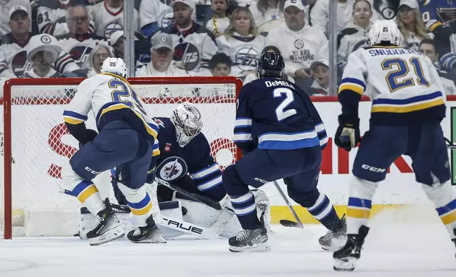 Winnipeg Jets goaltender Connor Hellebuyck, second from left, saves a breakaway shot by St. Louis Blues' Jordan Kyrou (25) during second-period NHL hockey playoff action in Winnipeg, Manitoba, Saturday, April 19, 2025. (John Woods/The Canadian Press via AP)