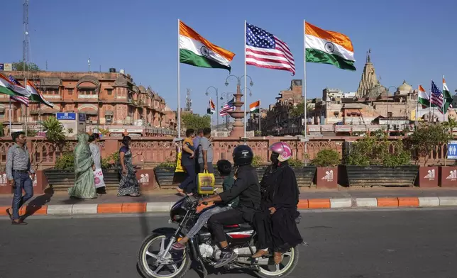 A family on a motorcycle watches Indian and US flags put up ahead of the US Vice President JD Vance visit in Jaipur, India, Monday, April 21, 2025. (AP Photo/Manish Swarup)