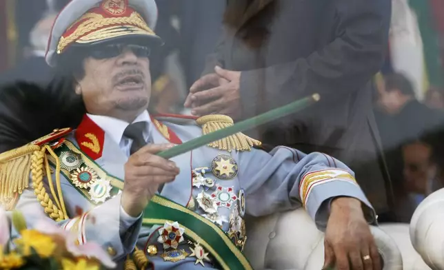FILE - Libyan leader Moammar Gadhafi gestures with a green cane as he takes his seat behind bulletproof glass for a military parade on Sept. 1, 2009, in Green Square, Tripoli, Libya. (AP Photo/Ben Curtis, File)