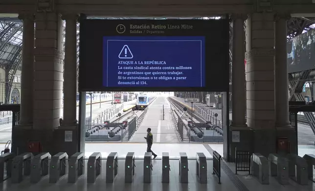 A lone worker walks through the Retiro train station that is empty due to a general strike against the austerity measures of President Javier Milei in Buenos Aires, Argentina, Thursday, April 10, 2025. The sign reads in Spanish "The unions attack millions of Argentines who want to work. If they extort you or force you to join the strike, report it to 134," and is a message to commuters from the government. (AP Photo/Rodrigo Abd)