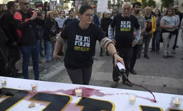 A relative of a hostage held in the Gaza Strip pours wine over a table as she takes part in a protest demanding immediate release of the hostages from Hamas captivity, during the Jewish holiday of Passover, in Tel Aviv, Israel, Saturday, April 12, 2025. (AP Photo/Leo Correa)