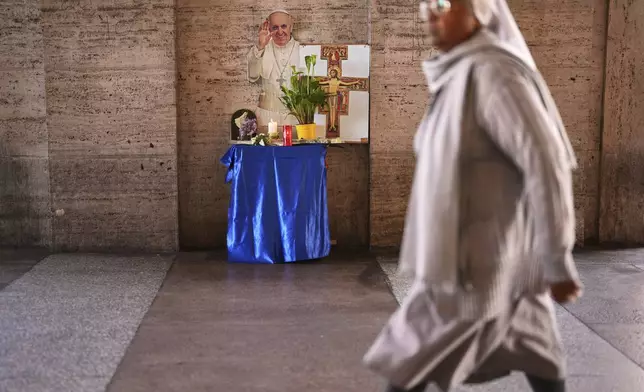 A cardboard cutout of the late Pope Francis is placed next to candles and flowers outside St. Peter's Square at the Vatican, Tuesday, April 22, 2025. (AP Photo/Francisco Seco)