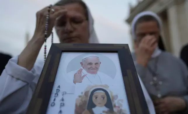 A nun holds a rosary and a picture of Pope Francis during a rosary prayer for the late Pope Francis, in St. Peter's Square at the Vatican, Tuesday April 22, 2025. (AP Photo/Bernat Armangue)
