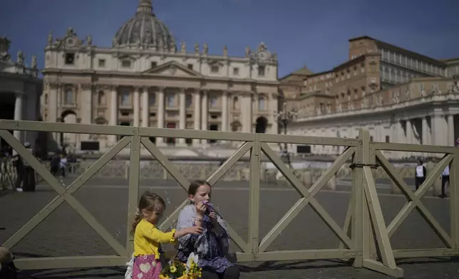 Margaret, left, and Sara from Slovakia sit at St. Peter's Square in front of St. Peter's Basilica where the body of Pope Francis will lie in state for three days, Wednesday, April 23, 2025. (AP Photo/Markus Schreiber)