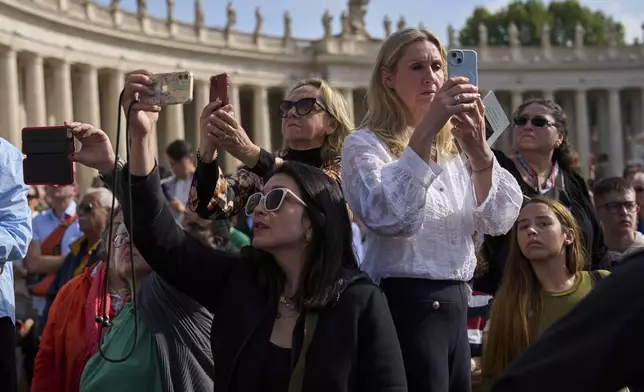 People take pictures in St. Peter's Square as the ceremony with the Pope Francis' body, who will lie in state for three days, arrives at St. Peter's Basilica in Vatican, Wednesday, April 23, 2025. (AP Photo/Bernat Armangue)