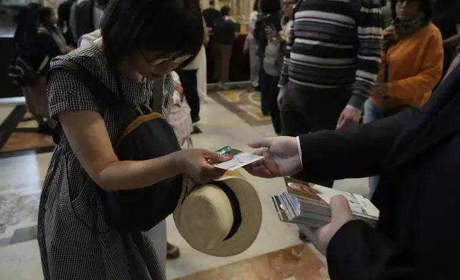 Faithful are given images of Pope Francis as they pay their respects to the late pontiff inside St. Peter's Basilica at the Vatican, Wednesday, April 23, 2025, where his body will lie in state for three days. (AP Photo/Gregorio Borgia)