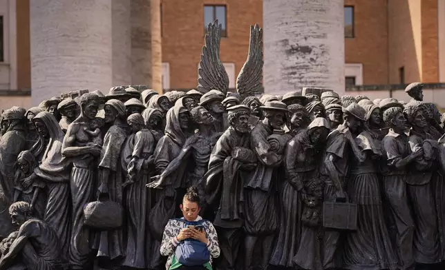 A woman sits on the Angels Unawares sculpture by Canadian artist Timothy P. Schmalz, which was was inaugurated by the late Pope Francis and depicts migrants and refugees throughout history, in St. Peter's Square as people wait to pay their respects at the Pontiff's coffin at St. Peter's Basilica, at the Vatican, Wednesday, April 23, 2025. (AP Photo/Andreea Alexandru)
