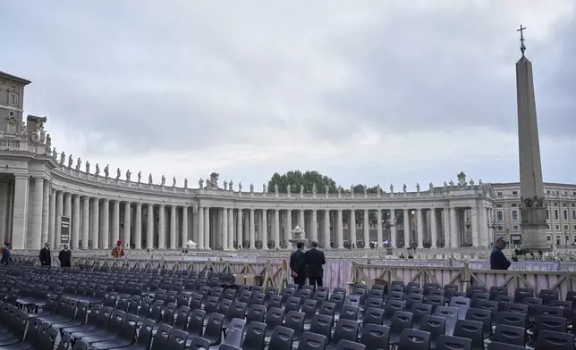 Two men stand near chairs during the preparations in St. Peter's Square ahead of the arrival of the body of Pope Francis, who will lie in state at St. Peter's Basilica for three days, at the Vatican, Wednesday, April 23, 2025. (AP Photo/Alessandra Tarantino)