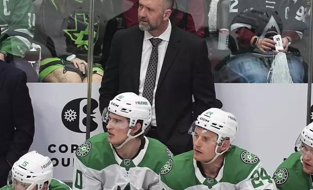 Dallas Stars head coach Peter DeBoer, back, looks on from the team box in the first period of Game 3 of an NHL hockey first-round playoff series against the Colorado Avalanche Wednesday, April 23, 2025, in Denver. (AP Photo/David Zalubowski)