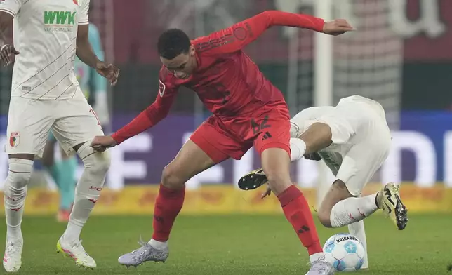 Augsburg's Alexis Claude Maurice falls by Bayern's Jamal Musiala during the German Bundesliga soccer match between Augsburg and Bayern Munich in Augsburg, Friday, April 4, 2025. (AP Photo/Matthias Schrader)