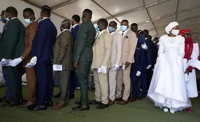 Groomsmen queue to collect their partner's flower bouquet inside a marquee ahead of the mass Easter weddings for 3,000 people, some polygamous, at the International Pentecost Holiness Church in Heidelberg, east of Johannesburg, South Africa, Sunday, April 20, 2025. (AP Photo/Themba Hadebe)