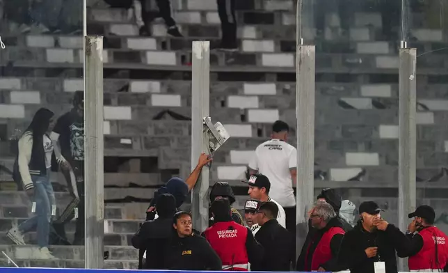 Security stewards confront fans after glass panels were broken and people invaded the field during a Copa Libertadores Group E soccer match against Brazil's Fortaleza at Monumental Stadium in Santiago, Chile, Thursday, April 10, 2025. (AP Photo/Esteban Felix)