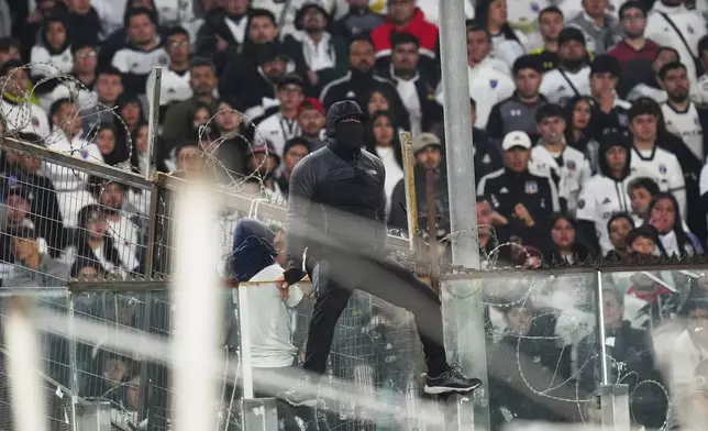 A fan climbs on a glass panel in the stands during a Copa Libertadores Group E soccer match between Chile's Colo Colo and Brazil's Fortaleza at Monumental Stadium in Santiago, Chile, Thursday, April 10, 2025. (AP Photo/Esteban Felix)