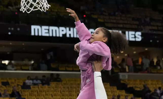 Memphis Grizzlies guard Ja Morant helps his daughter Kaari Morant shoot a basket before an NBA play-in tournament basketball game against the Dallas Mavericks, Friday, April 18, 2025, in Memphis, Tenn. (AP Photo/George Walker IV)