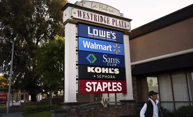 A person walks past a cluster of retail store signs in La Habra, Calif., Wednesday, April 2, 2025. (AP Photo/Jae C. Hong)