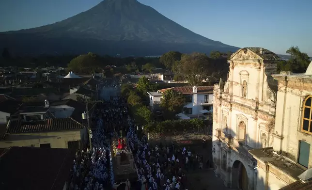 Penitents knows as "cucuruchos" carry a statue of Jesus Christ bearing a cross, during a Holy Week procession in Antigua, Guatemala on Good Friday, April 18, 2025. The "Volcan de Agua," or Water Volcano, stands behind. (AP Photo/Moises Castillo)