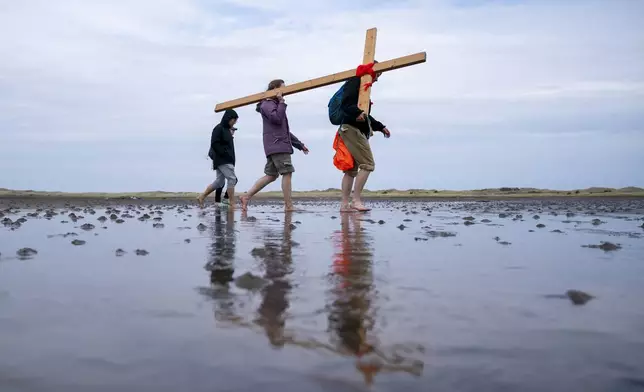 Pilgrims carry wooden crosses on Good Friday across the sands at low tide to the Holy Island of Lindisfarne, in Northumberland, north England, during the annual Christian Easter pilgrimage, Friday April 18, 2025. (Jane Barlow/PA via AP)