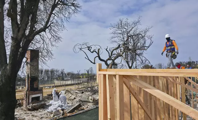 A worker stands atop a home being rebuilt after the Palisades Fire in the Pacific Palisades neighborhood of Los Angeles, Thursday, April 24, 2025. (AP Photo/Damian Dovarganes)