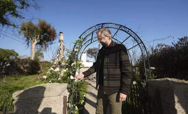Tim Vordtriede holds white roses at the gate of his property, which was destroyed the Eaton Fire in Altadena, Calif., on Tuesday, April 22, 2025. (AP Photo/Damian Dovarganes)