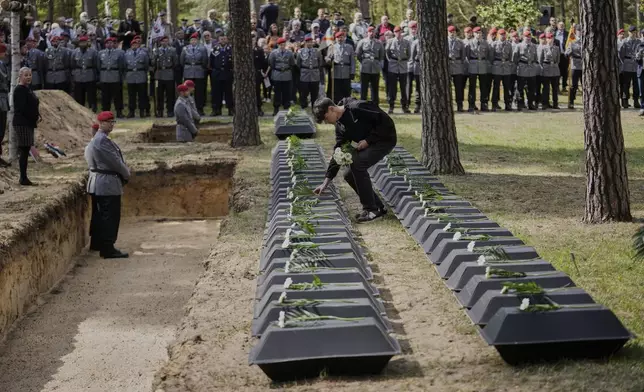 A student pays tribute to the small coffins with the remains of fallen German soldiers of WWII during a funeral service at a memorial site for fallen soldiers in Halbe, Germany, Wednesday, April 30, 2025. (AP Photo/Ebrahim Noroozi)