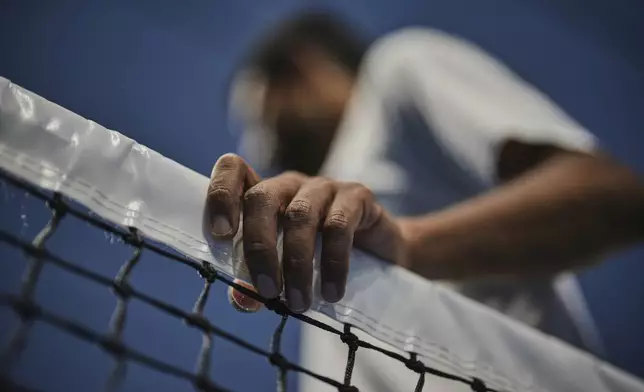Blind tennis champion Naqi Rizvi holds onto the net during a visually impaired tennis training session in London, Tuesday, May 20, 2025. (AP Photo/Kin Cheung)