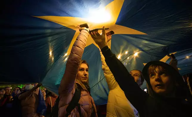Demonstrators shine the lights of their mobile phones as they stand under a large European Union flag, during a pro-EU rally ahead of the second round of the presidential election redo in Bucharest, Romania, Friday, May 9, 2025. (AP Photo/Andreea Alexandru)