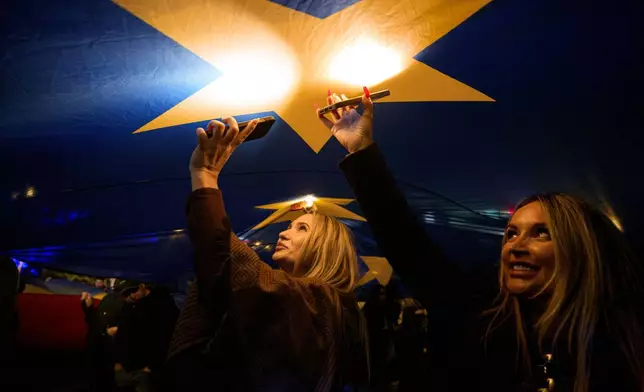 People shine the lights of their mobile phones standing under a large European Union during a pro-EU rally ahead of the second round of the presidential election redo in Bucharest, Romania, Friday, May 9, 2025. (AP Photo/Andreea Alexandru)