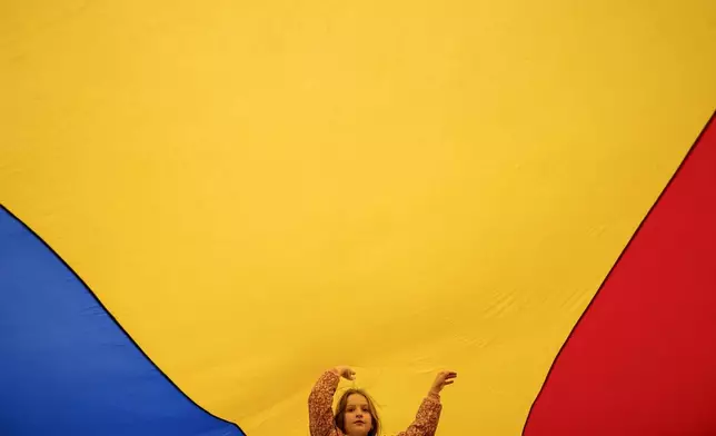 A child plays under a large Romanian flag during a Pro-EU rally ahead of the second round of the presidential election redo in Bucharest, Romania, Friday, May 9, 2025. (AP Photo/Andreea Alexandru)
