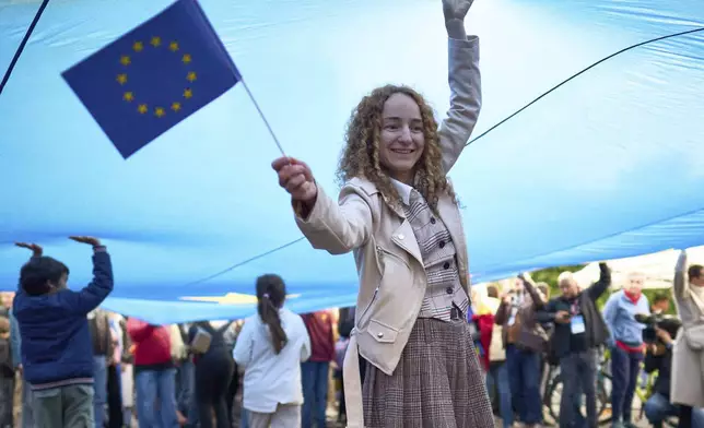Corina Chirila stands under an European Union flag during a pro-EU rally ahead of the second round of the presidential election redoin Bucharest, Romania, Friday, May 9, 2025. (AP Photo/Vadim Ghirda)