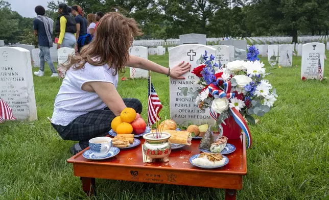 FILE - Kim Hoan Nguyen, of Falls Church, Va., who is originally from Vietnam, touches her son's gravestone next to ritual offerings in the Vietnamese tradition at the gravesite of her son, Marine Corporal Binh N Le, who died serving in Iraq in 2004, in Section 60 of Arlington National Cemetery, in Arlington, Va., Monday, May 27, 2024, on Memorial Day. (AP Photo/Jacquelyn Martin, File)