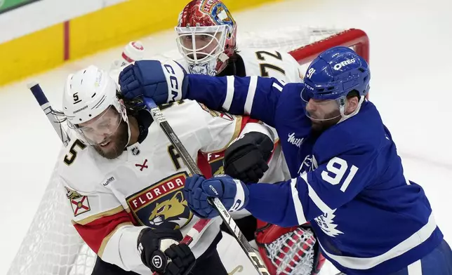 Toronto Maple Leafs' John Tavares (91) hits Florida Panthers' Aaron Ekblad (5) in front of teammate Sergei Bobrovsky (72) during third period NHL playoff hockey action in Toronto on Wednesday, May 14, 2025. Tavares received a roughing penalty on the play. (Frank Gunn/The Canadian Press via AP)