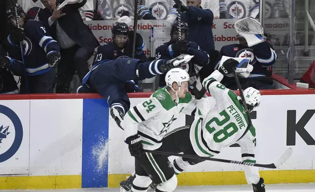 Dallas Stars' Alexander Petrovic (28) checks Winnipeg Jets' Adam Lowry, center, into the bench during the second period of Game 2 of a second-round NHL hockey playoff series in Winnipeg, Manitoba, Friday, May 9, 2025. (Fred Greenslade/The Canadian Press via AP)