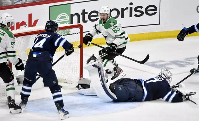 Winnipeg Jets goaltender Connor Hellebuyck, bottom right, gets a piece of the puck to deflect a shot by Dallas Stars' Evgenii Dadonov (63) during the second period of Game 2 of a second-round NHL hockey playoff series in Winnipeg, Manitoba, Friday, May 9, 2025. (Fred Greenslade/The Canadian Press via AP)