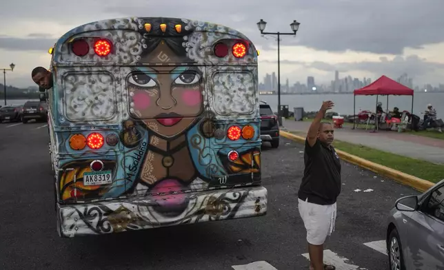 The driver of a Red Devil tourist bus calls for customers along the Amador Causeway in Panama City, Sunday, Sept. 15, 2024. The Red Devils are former U.S. school buses once used in the Panama Canal Zone and later as public transport or adapted for private and cultural use. (AP Photo/Matias Delacroix)
