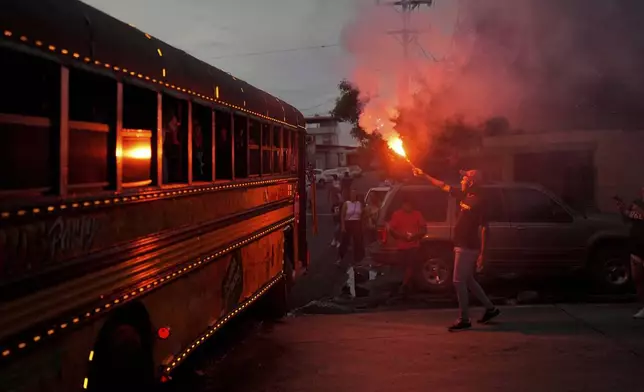 A man illuminates with flare a Red Devil party bus in Panama City, Sunday, Aug. 25, 2024. The Red Devils are repurposed U.S. school buses once used in the Panama Canal Zone and later as public transport, now adapted for private and cultural use. (AP Photo/Matias Delacroix)