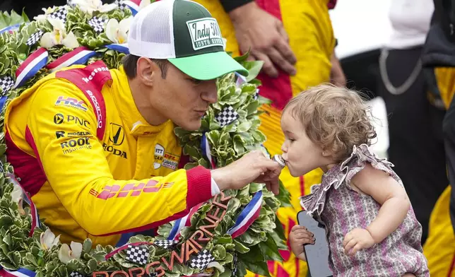Alex Palou, left, of Spain, has his winner's ring kissed by his daughter Lucia on the Yard of Bricks on the start/finish line after winning the Indianapolis 500 auto race at Indianapolis Motor Speedway in Indianapolis, Sunday, May 25, 2025. (AP Photo/AJ Mast)