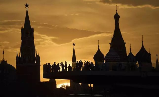 People watch and photograph sunset behind the Kremlin standing on the "Flying glass bridge" over the Moscow River at Zaryadye park in Moscow, Russia, Thursday, May 29, 2025. (AP Photo/Alexander Zemlianichenko)