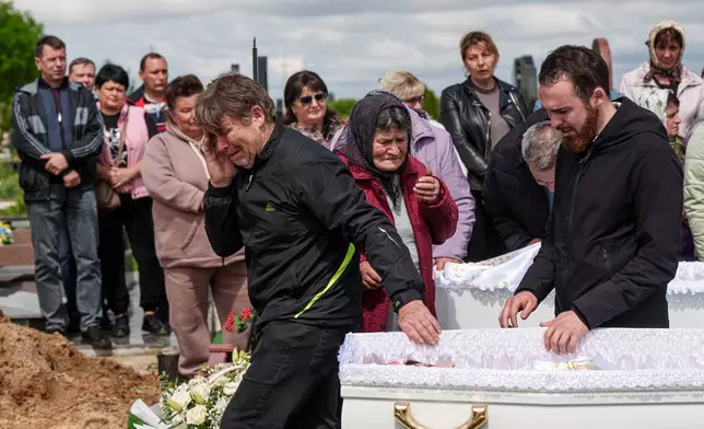 A father, left, mourns his children Tamara Martyniuk, 8, Stanislav Martyniuk, 12, and Roman Martyniuk, 17, killed in a Russian strike on Sunday, during farewell ceremony in Korostyshiv, Zhytomyr region, Ukraine, Wednesday, May 28, 2025. (AP Photo/Evgeniy Maloletka)