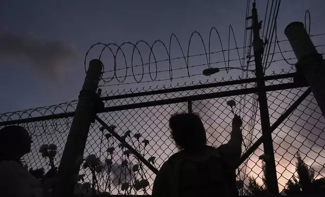 People place flowers on a fence outside Krome Detention Center in Miami, Saturday, May 24, 2025, during a vigil to recognize people who have died in U.S. Immigration and Customs Enforcement custody as well as those affected by mass deportations. (AP Photo/Rebecca Blackwell)