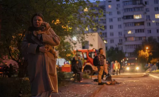 A woman carries her dog as she walks on a street with pieces of broken glass at the site of a residential building that was damaged after a Russian attack in Kyiv, Ukraine, Saturday, May 24, 2025. (AP Photo/Alex Babenko)