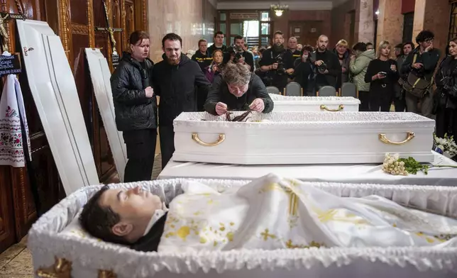 A father, center, mourns his children Tamara Martyniuk, 8, Stanislav Martyniuk, 12, and Roman Martyniuk, 17, killed in a Russian strike on Sunday, during farewell ceremony in Korostyshiv, Zhytomyr region, Ukraine, Wednesday, May 28, 2025. (AP Photo/Evgeniy Maloletka)