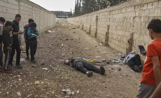 EDS NOTE: GRAPHIC CONTENT - Syrian boys look at the bodies of the former Shanaya's town mayor Houssam Warawar and his son Haidar, who were killed in the town of Sahnaya, south of Damascus, Syria, Thursday, May 1, 2025, a day after clashes erupted between members of the minority Druze sect and pro-government fighters. (AP Photo/Ghaith Alsayed)