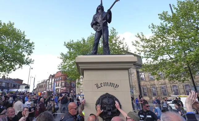 Motorhead fans touch the Motorhead logo to commemorate Lemmy Kilmister the former Motorhead frontman in Burslem, Stoke on Trent, England, Friday, May 9, 2025. The musician, once described as having 'one of the most recognizable voices in rock', was born in Burslem and a statue has been crafted by acclaimed local sculptor and lifelong Motorhead fan Andy Edwards. (AP Photo/Kirsty Wigglesworth)