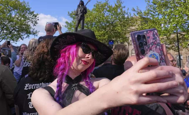 A fan takles a selfie with the statue in background as Motorhead fans gather to commemorate Lemmy Kilmister the Motorhead frontman in Burslem, Stoke on Trent, England, Friday, May 9, 2025. The musician, once described as having 'one of the most recognizable voices in rock', was born in Burslem and a statue has been crafted by acclaimed local sculptor and lifelong Motorhead fan Andy Edwards. (AP Photo/Kirsty Wigglesworth)