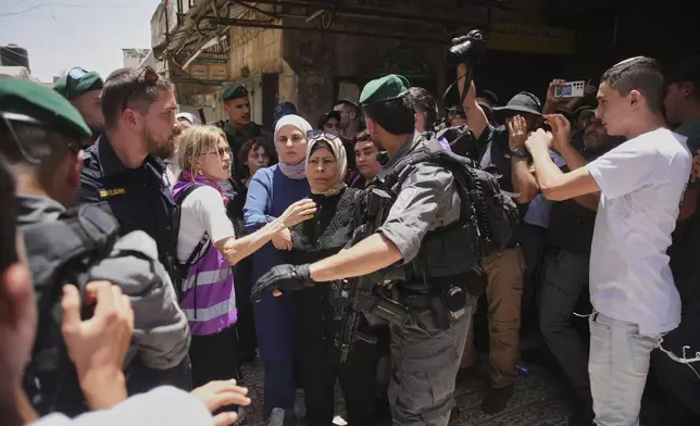 Israeli police officers escort Palestinian women while Israelis marking Jerusalem Day, an Israeli holiday celebrating the capture of east Jerusalem in the 1967 Mideast war, in Jerusalem's Old City, Monday, May 26, 2025. (AP Photo/Ohad Zwigenberg)