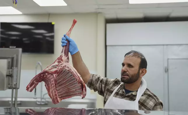 Shahpoor Essazada, a butcher at the Finest Supermarket halal grocery store in Fredericksburg, Va., holds up a piece of meat for a customer, on Monday, April 7, 2025. (AP Photo/Jessie Wardarski)