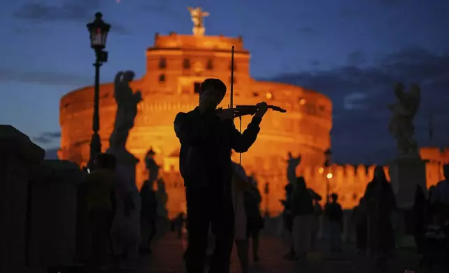 A street musician plays a violin outside the Sant'Angelo castle as the sun sets in Rome, Sunday, May 4, 2025. (AP Photo/Francisco Seco)