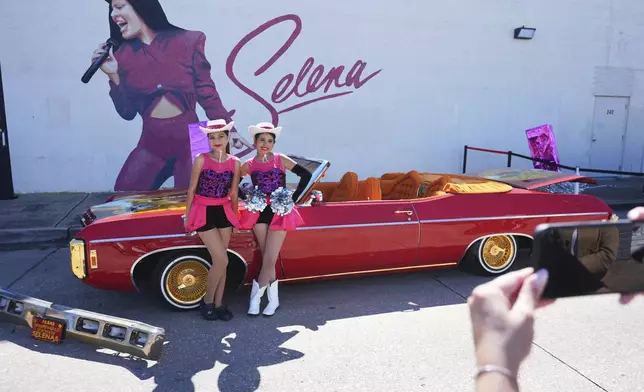 Eleven-year-olds Kataleah Mendez, right, and Angelica Juarez pose for a photo with the low rider car that appeared in the movie Selena parked for display during a Cinco de Mayo celebration in the Oak Cliff section of Dallas, Saturday, May 3, 2025. (AP Photo/LM Otero)
