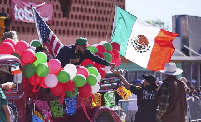 A float rider hands candy to a Dallas police officer during a Cinco de Mayo parade in the Oak Cliff section of Dallas, Saturday, May 3, 2025. (AP Photo/LM Otero)