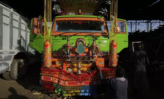 A worker affixes decorated metal pieces on a newly refurbished truck at a yard for workshops in Rawalpindi, Pakistan, Tuesday, April 22, 2025. (AP Photo/Anjum Naveed)